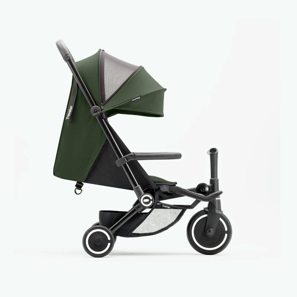 Vista lateral del coche triciclo SmarTrike Traveler verde desplegado en modo paseo, mostrando toldo, respaldo reclinable, barra delantera, canasta de almacenamiento inferior con malla y tres ruedas con aros blancos. Fondo verde muy claro.