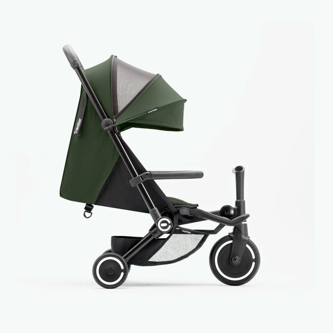Vista lateral del coche triciclo SmarTrike Traveler verde desplegado en modo paseo, mostrando toldo, respaldo reclinable, barra delantera, canasta de almacenamiento inferior con malla y tres ruedas con aros blancos. Fondo verde muy claro.