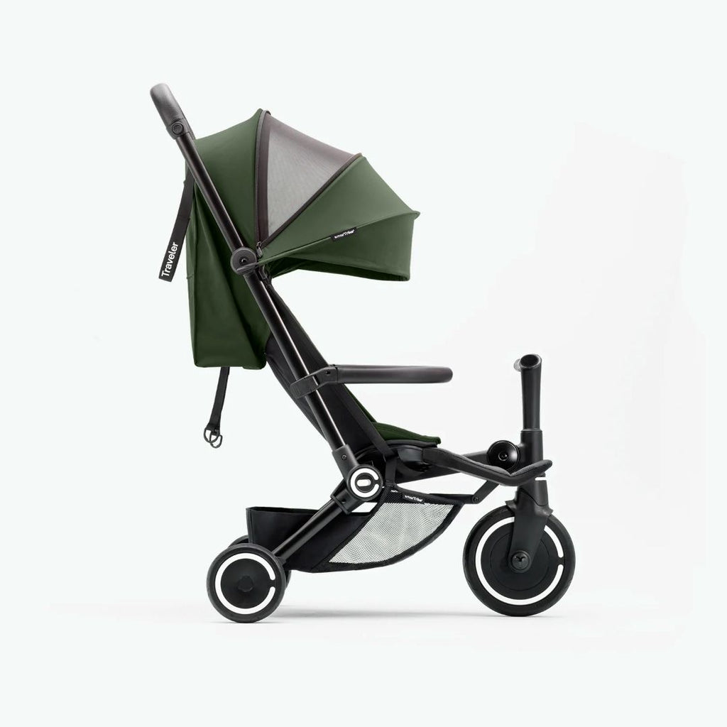 Vista lateral del coche triciclo SmarTrike Traveler verde en modo paseo con toldo desplegado, respaldo vertical y canasta inferior, sobre fondo verde muy claro.