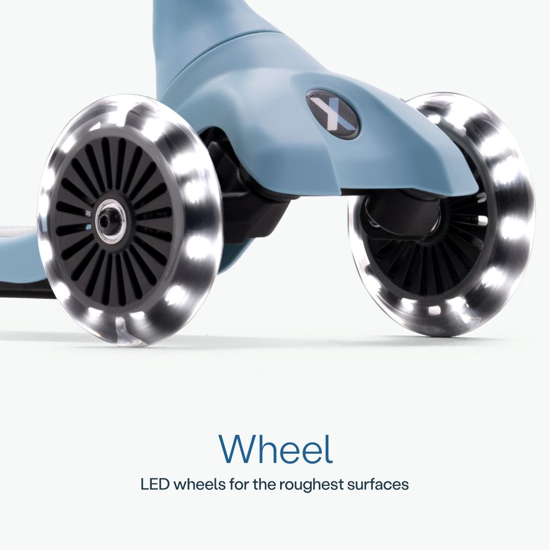 Detalle en primer plano de las dos ruedas delanteras con luz LED del scooter SmarTrike Xtend Mini+ Celeste y logo Xtend visible. Texto: "Wheel. LED wheels for the roughest surfaces." Fondo azul muy claro.
