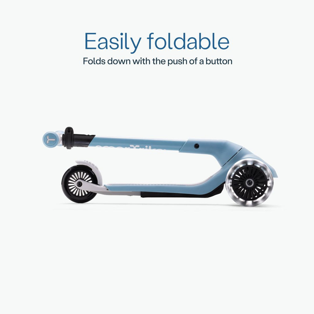 Vista lateral del scooter SmarTrike Xtend Mini+ color Celeste completamente plegado en formato compacto, con ruedas LED visibles. Texto: "Easily foldable. Folds down with the push of a button." Fondo azul muy claro.