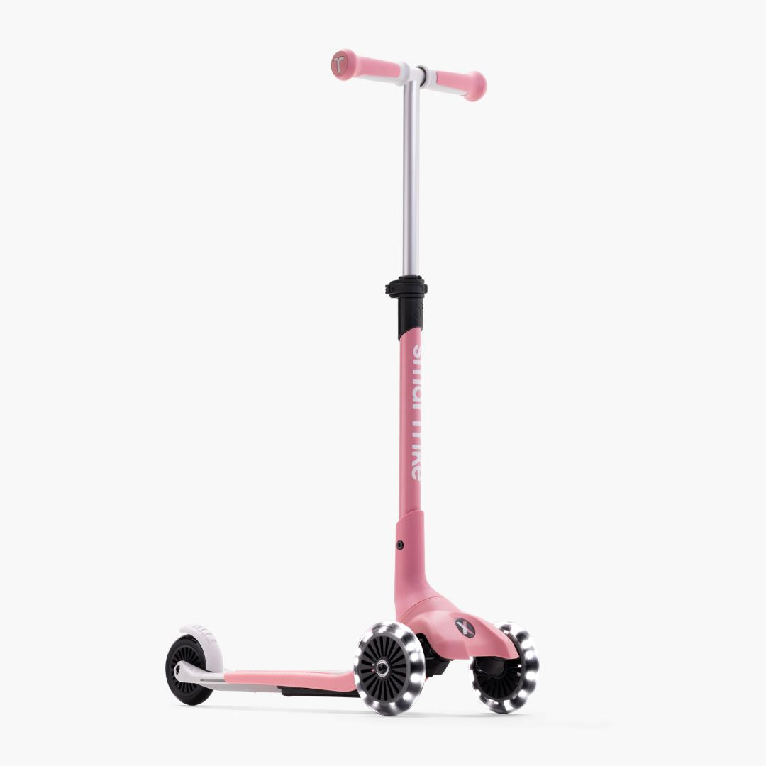 Vista lateral del scooter evolutivo SmarTrike Xtend Mini+ en color Palo Rosa con manubrio en T rosa, cuerpo rosa, estructura blanca y tres ruedas con luz LED. Fondo blanco.