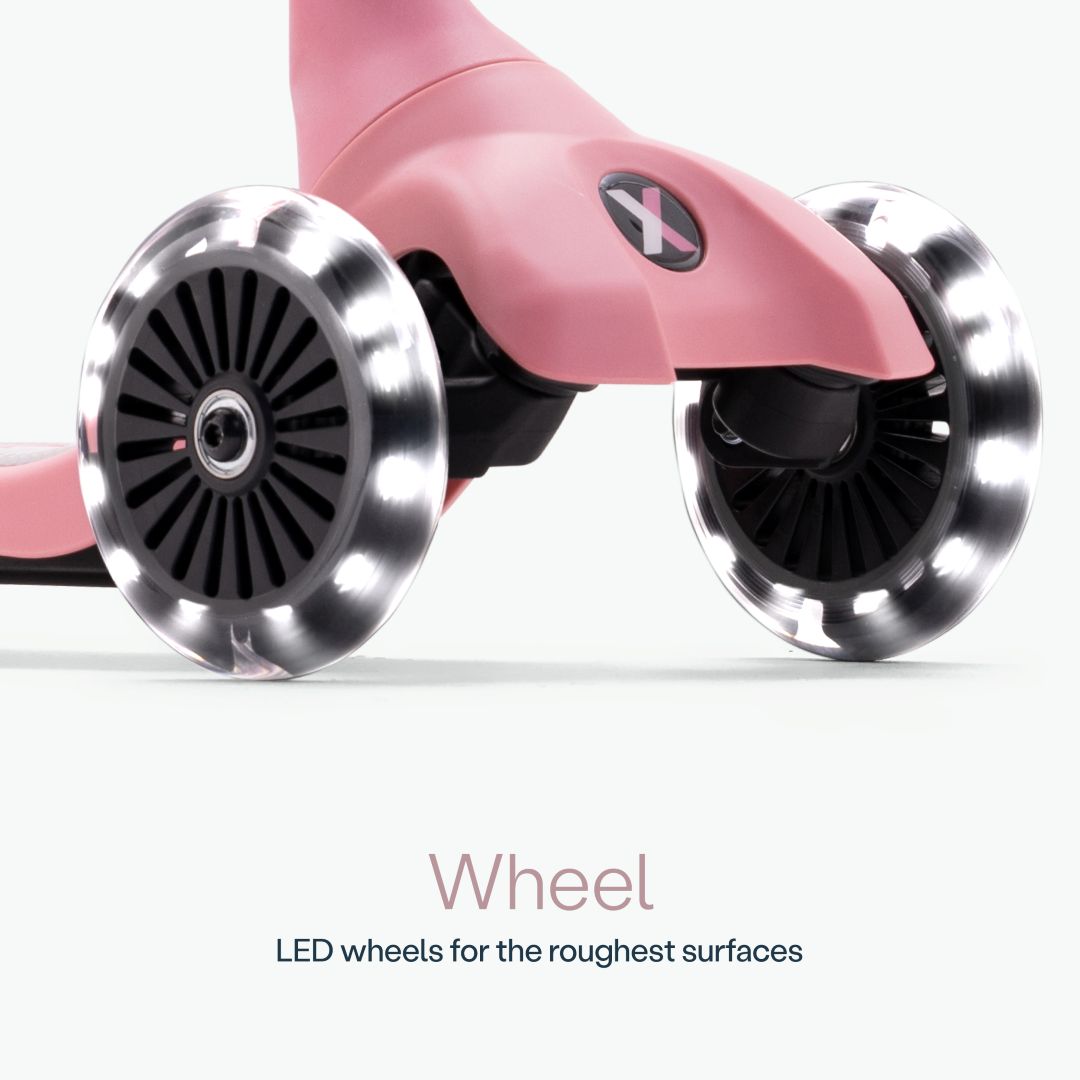 Detalle en primer plano de las dos ruedas delanteras con luz LED del scooter SmarTrike Xtend Mini+ Palo Rosa y logo Xtend visible. Texto: "Wheel. LED wheels for the roughest surfaces." Fondo gris muy claro.
