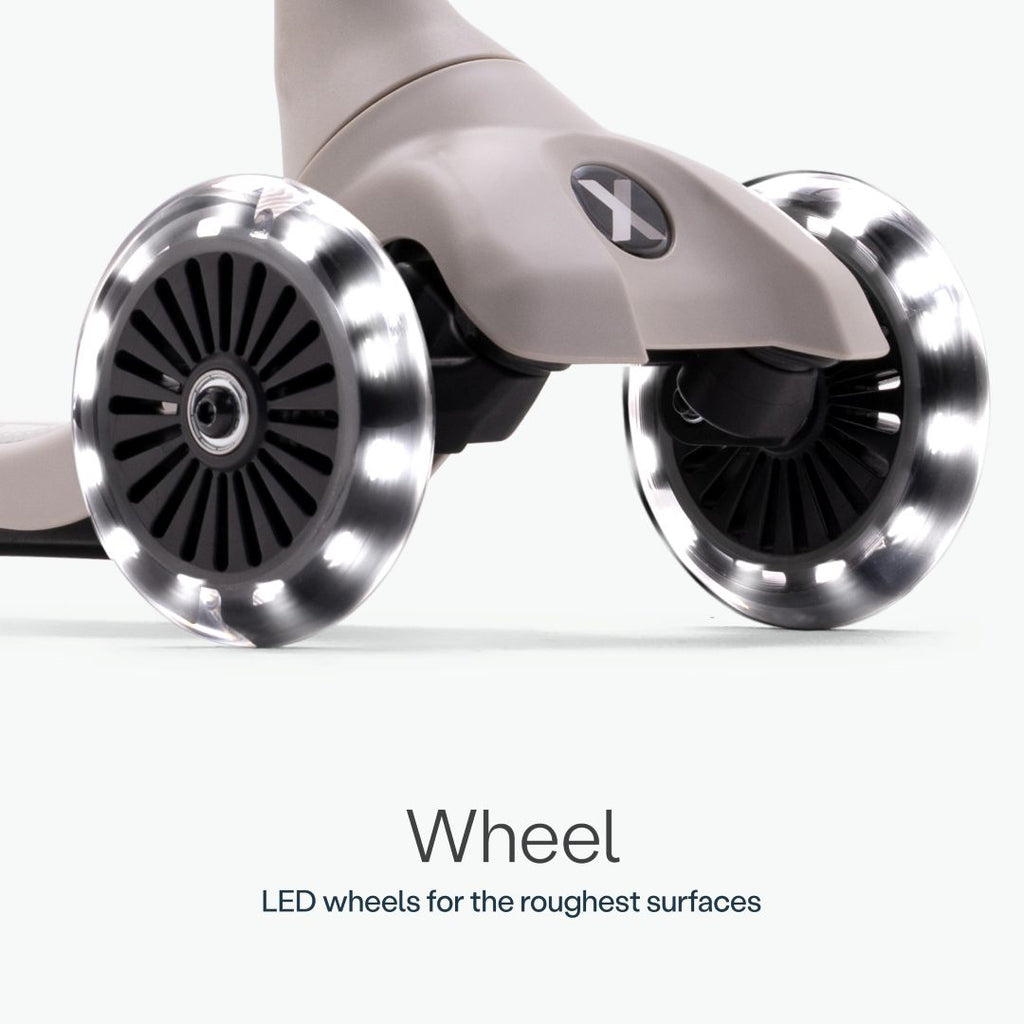 Detalle en primer plano de las dos ruedas delanteras con luz LED del scooter SmarTrike Xtend Mini+ Gris y logo Xtend visible. Texto: "Wheel. LED wheels for the roughest surfaces." Fondo gris muy claro.