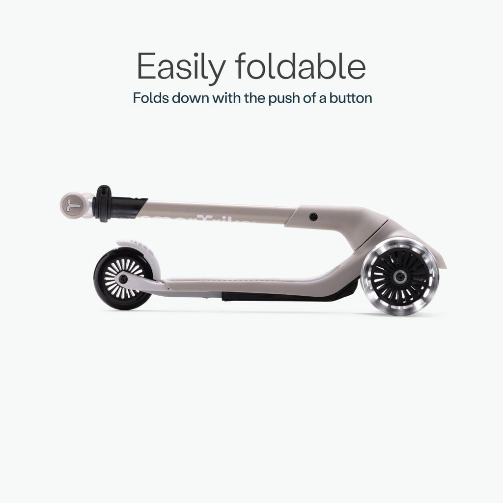 Vista lateral del scooter SmarTrike Xtend Mini+ color Gris completamente plegado en formato compacto, con ruedas LED visibles. Texto: "Easily foldable. Folds down with the push of a button." Fondo gris muy claro.