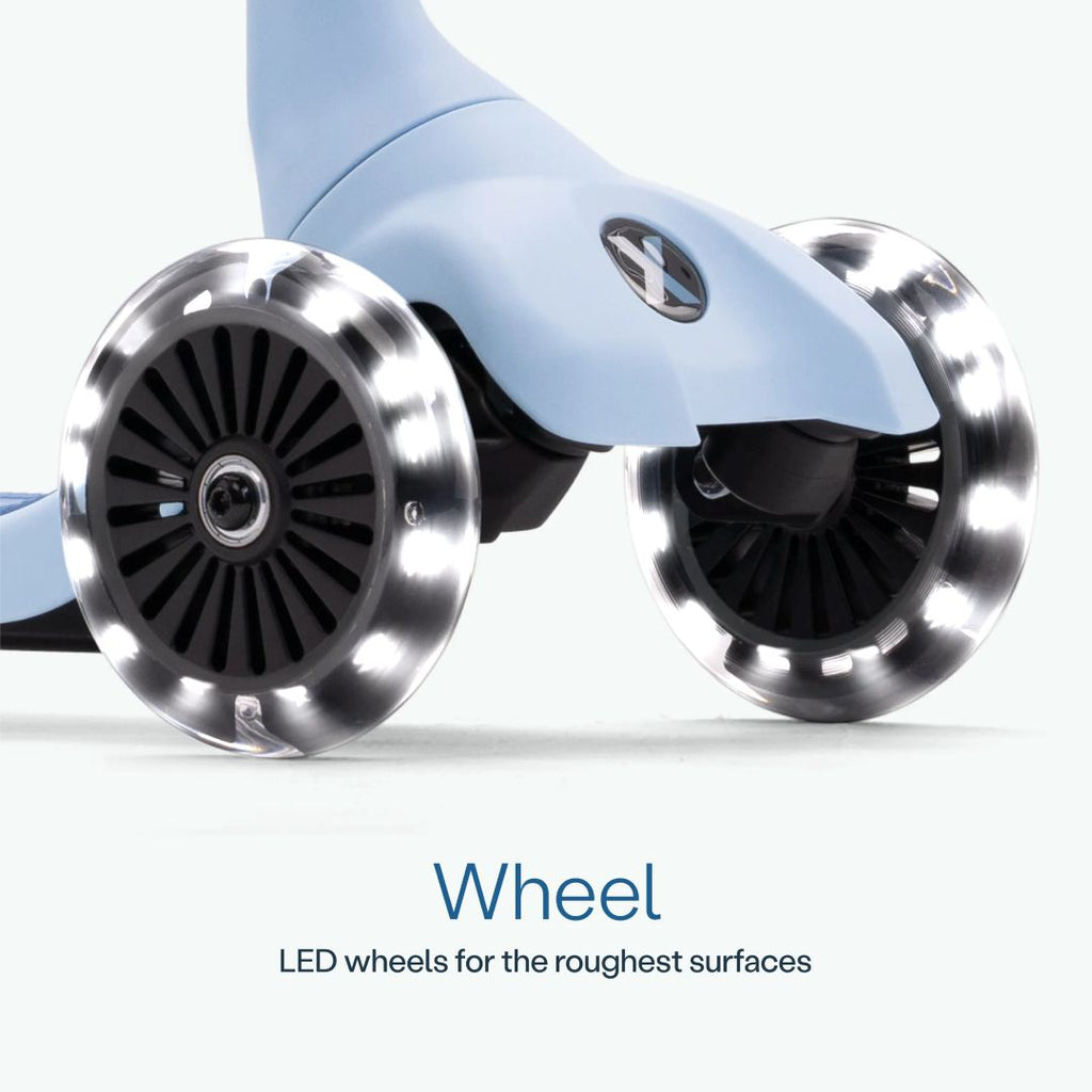 Detalle de las dos ruedas delanteras con luz LED del scooter SmarTrike Xtend Mini Ride en color Celeste, sobre fondo celeste claro. Texto: "Wheel. LED wheels for the roughest surfaces."