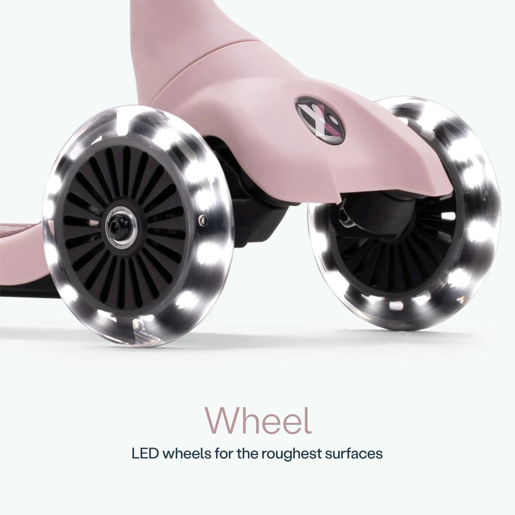 Detalle de las dos ruedas delanteras con luz LED del scooter SmarTrike Xtend Mini Ride en color Palo Rosa, sobre fondo verde claro. Texto: "Wheel. LED wheels for the roughest surfaces."