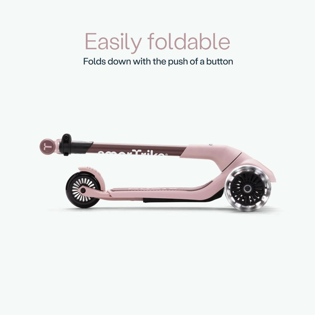 Vista lateral del scooter SmarTrike Xtend Mini Ride color Palo Rosa completamente plegado, mostrando su diseño compacto. Texto: "Easily foldable. Folds down with the push of a button."