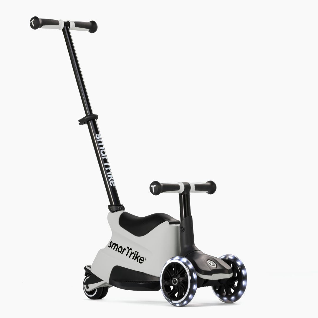 Vista frontal en ángulo del scooter evolutivo SmarTrike Xtend Ride-On Gris en modo ride-on, con asiento, manubrio para niño, barra para padres inclinada y tres ruedas con luz LED. Fondo blanco.