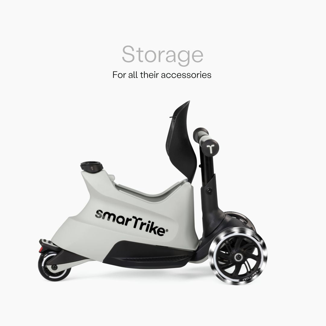 Vista lateral del scooter SmarTrike Xtend Ride-On Gris en modo ride-on mostrando el compartimento de almacenamiento abierto bajo el asiento y ruedas LED. Texto: "Storage. For all their accessories." Fondo blanco.