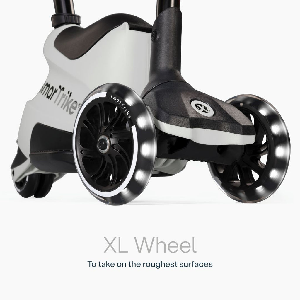 Detalle en primer plano de las ruedas XL con luz LED del scooter evolutivo SmarTrike Xtend Ride-On Gris, con cuerpo gris y negro y logo de la marca. Texto: "XL Wheel. To take on the roughest surfaces." Fondo blanco.