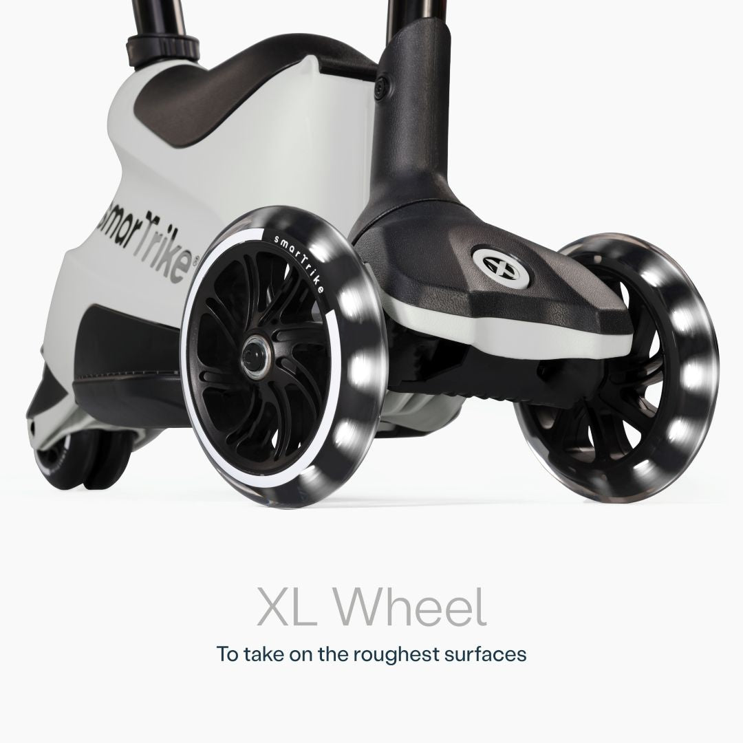 Detalle en primer plano de las ruedas XL con luz LED del scooter evolutivo SmarTrike Xtend Ride-On Gris, con cuerpo gris y negro y logo de la marca. Texto: "XL Wheel. To take on the roughest surfaces." Fondo blanco.