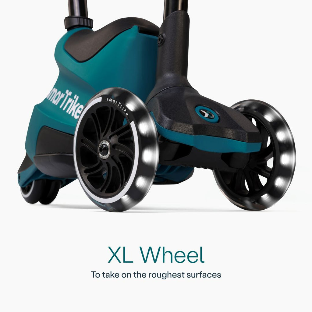 Detalle en primer plano de las ruedas XL con luz LED del scooter evolutivo SmarTrike Xtend Ride-On Petróleo, con cuerpo gris y negro y logo de la marca. Texto: "XL Wheel. To take on the roughest surfaces." Fondo blanco.