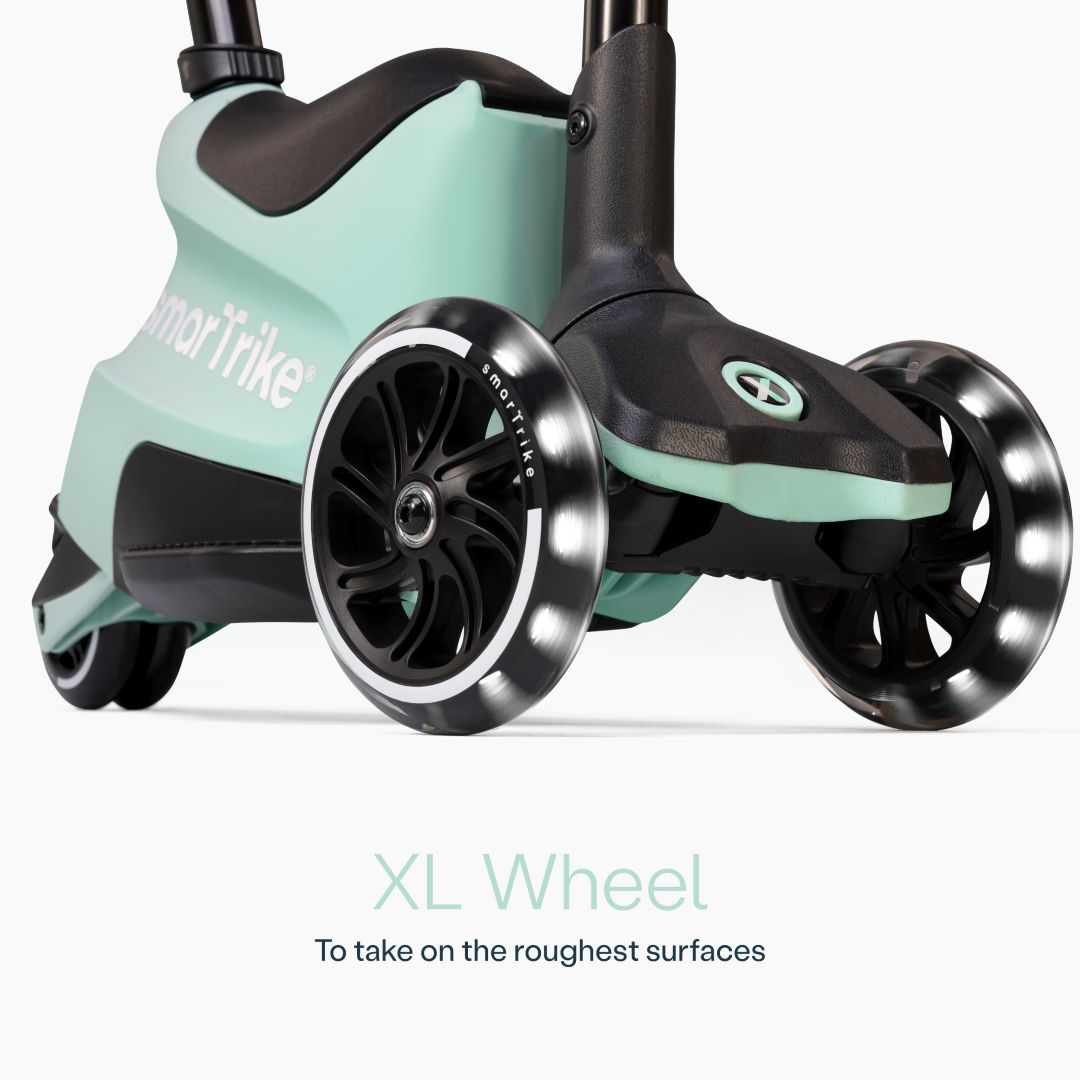 Detalle en primer plano de las ruedas XL con luz LED del scooter evolutivo SmarTrike Xtend Ride-On Verde Agua, con cuerpo gris y negro y logo de la marca. Texto: "XL Wheel. To take on the roughest surfaces." Fondo blanco.