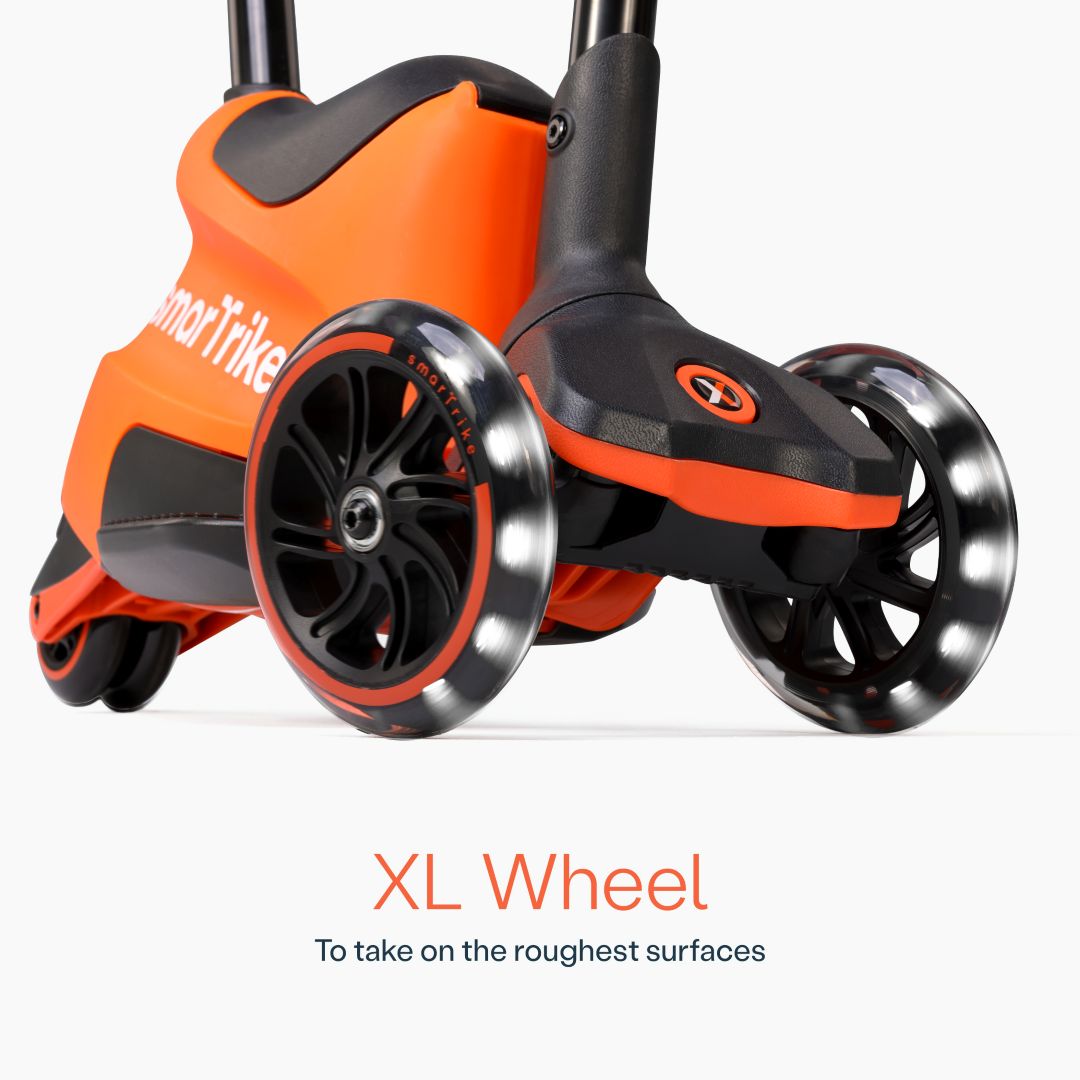 Detalle en primer plano de las ruedas XL con luz LED del scooter evolutivo SmarTrike Xtend Ride-On Naranjo, con cuerpo gris y negro y logo de la marca. Texto: "XL Wheel. To take on the roughest surfaces." Fondo blanco.