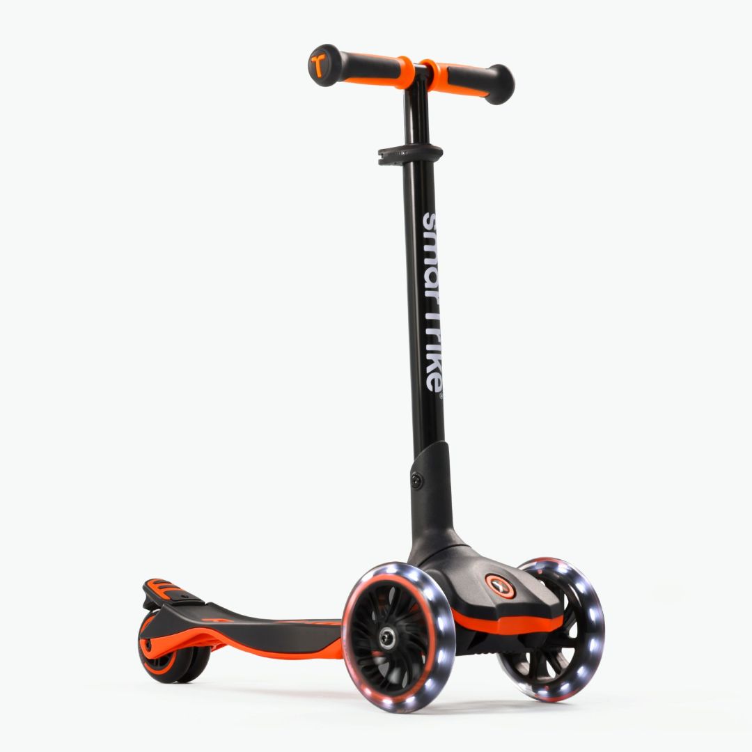 Vista frontal en ángulo del scooter evolutivo SmarTrike Xtend en color naranja, plataforma extensible patentado, tres ruedas XL con luz LED y plataforma antideslizante. Fondo gris claro.