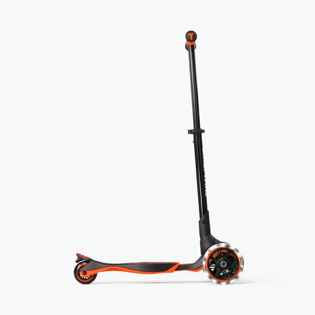 Vista lateral del scooter evolutivo SmarTrike Xtend naranja con manubrio extendido al máximo, plataforma  en posición avanzada y ruedas LED, en configuración para niños mayores. Fondo blanco