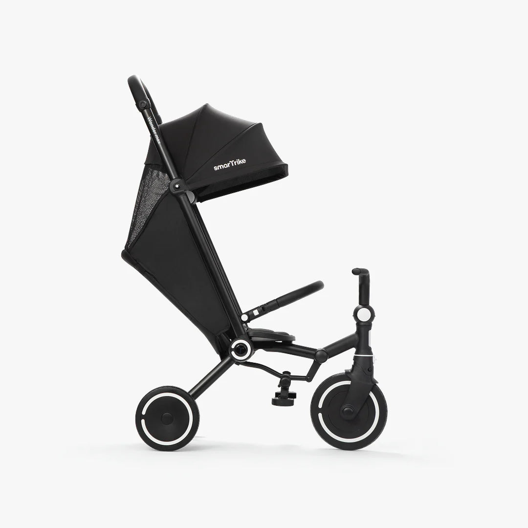 Coche triciclo evolutivo SmarTrike Wonder max color negro, plegable, apto para cabina de avión, uso desde los 6 meses, con dirección Easy-Steer 360° patentado, respaldo reclinable 140 grados, panel de malla transpirable, manubrio para padres, asiento con reposapiés y tres ruedas con aros blancos, fotografiado, en modo coche asiento reclinado, ángulo lateral sobre fondo blanco.