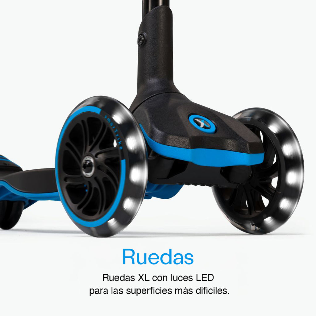 Detalle en primer plano de las tres ruedas XL con luz LED del scooter SmarTrike Xtend azul, con plataforma y detalles azules visibles. Texto: "Ruedas. Ruedas XL con luces LED para las superficies más difíciles." Fondo gris claro.